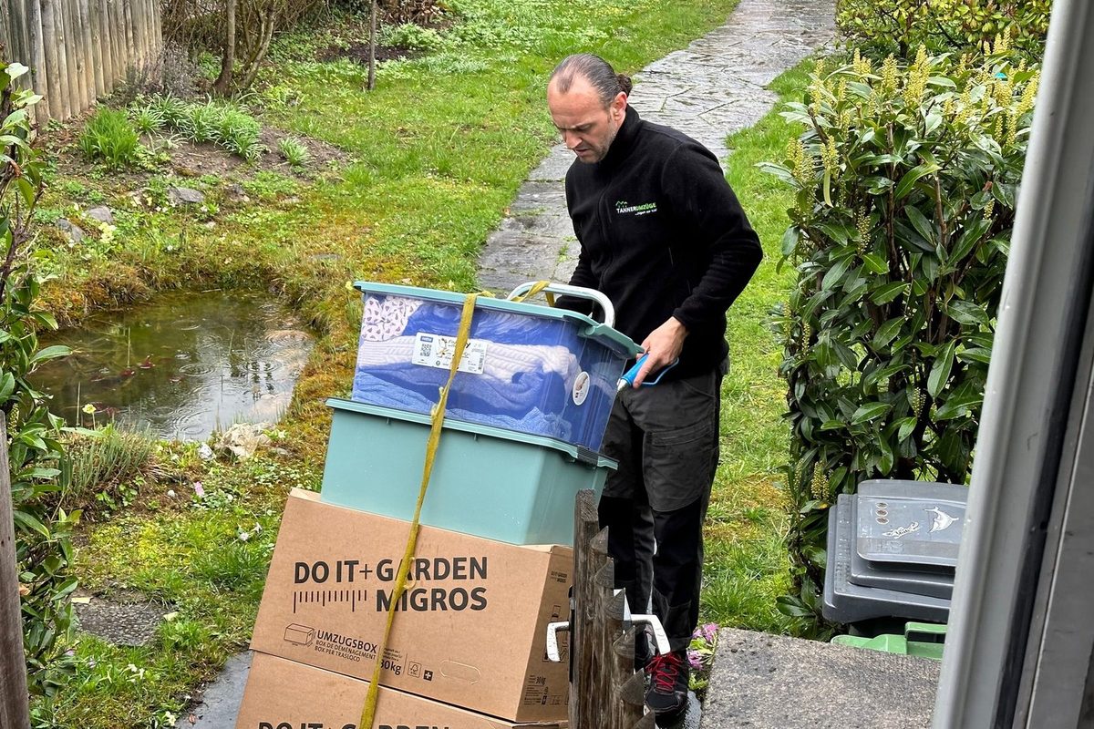Gestapelte Umzugskartons und Mehrwegboxen auf der Sackkarre eines Mitarbeiters von Tanner Umzüge