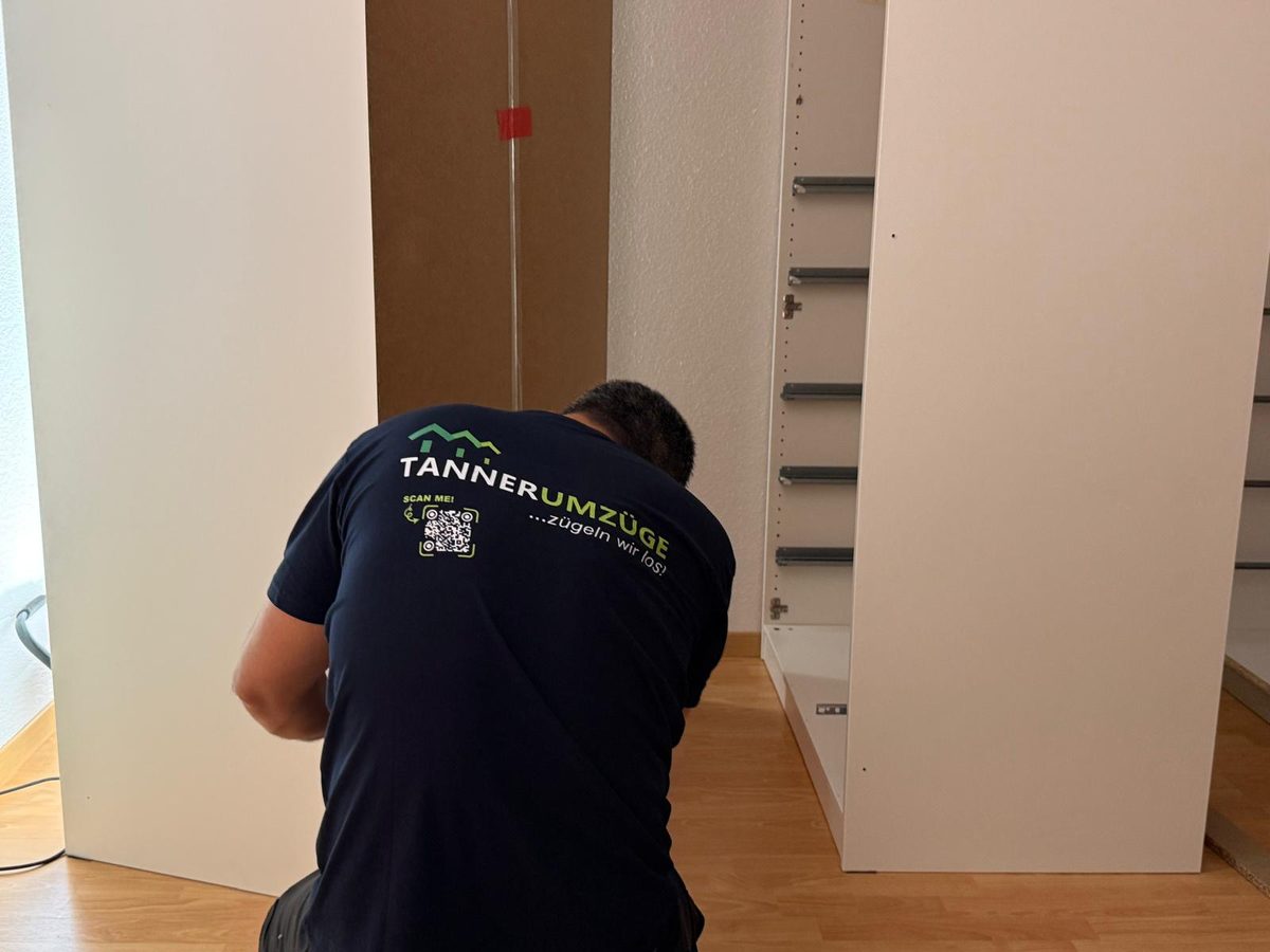 Umzugsfirma Kloten: Ein Mitarbeiter von Tanner Umzüge arbeitet an einem Kleiderschrank, auf dem Rücken das Logo von Tanner Umzüge