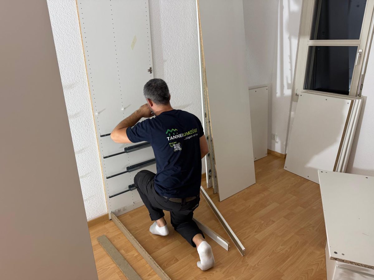 Ein Mitarbeiter von Tanner Umzüge kniet vor einem zerlegten Kleiderschrank und arbeitet an den Schubladenschienen